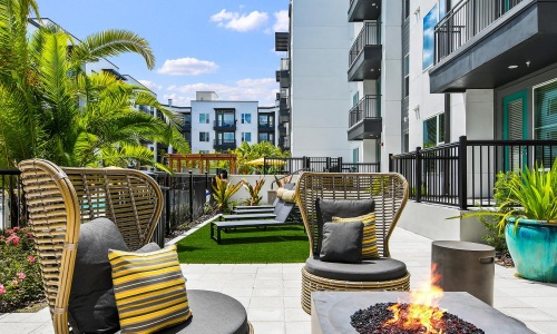 a patio with chairs and a fire pit with a fire in it